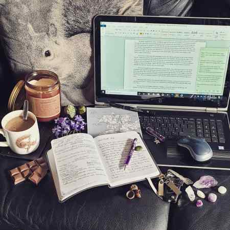 My writing tools - scented candle, hot chocolate, chocolate, laptop, pen, notebooks, bluebells, crystals, hand drawn map, and memory sticks